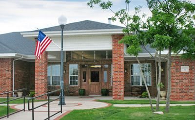 A brick building with an American flag, featuring a well-maintained lawn and trees.