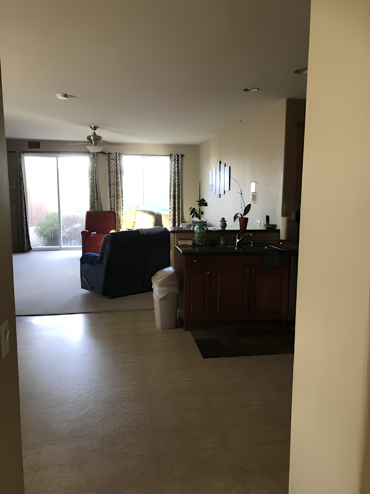 A view of a living room with a sofa, a kitchen counter, and large windows with curtains.