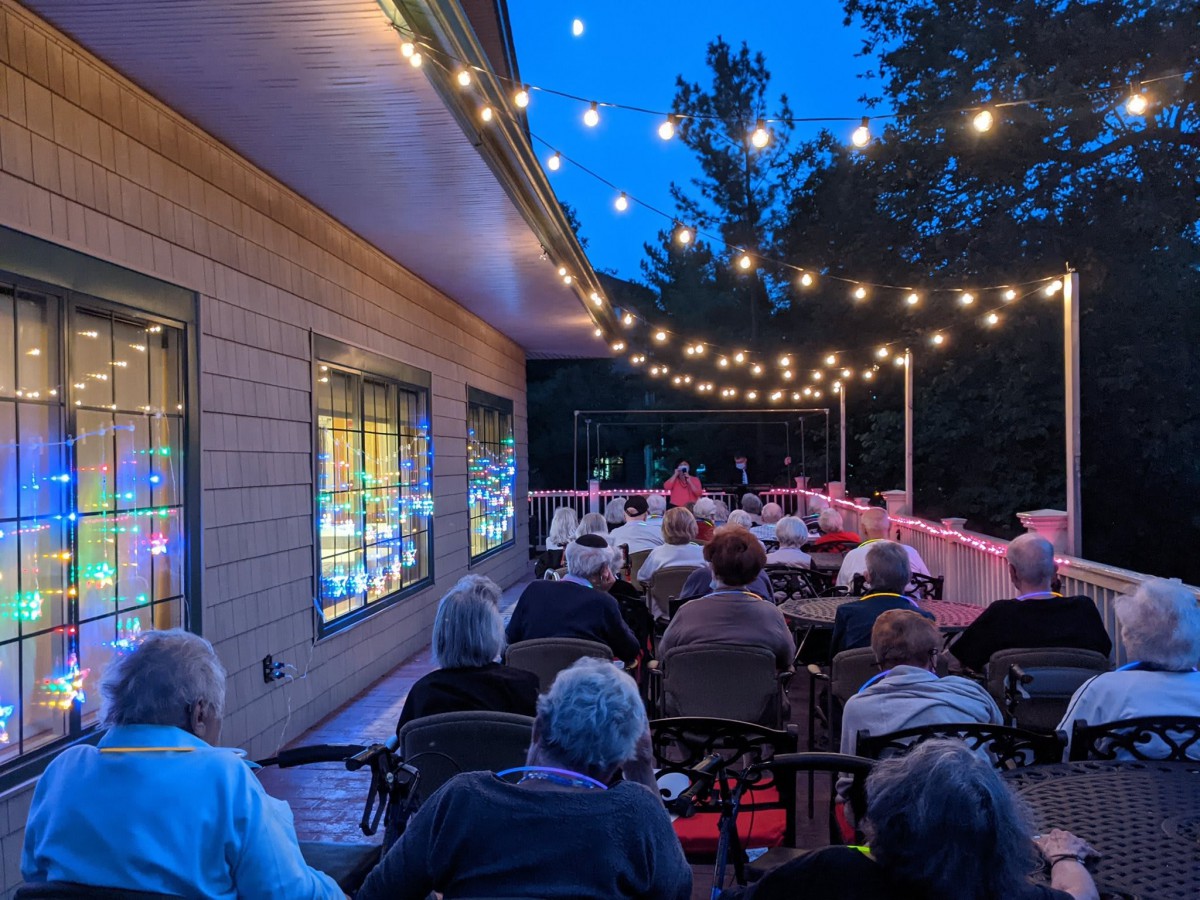 An outdoor evening gathering with people seated under string lights.