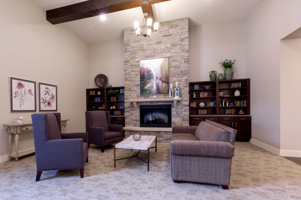 A cozy living room featuring a stone fireplace, armchairs, and bookshelves.