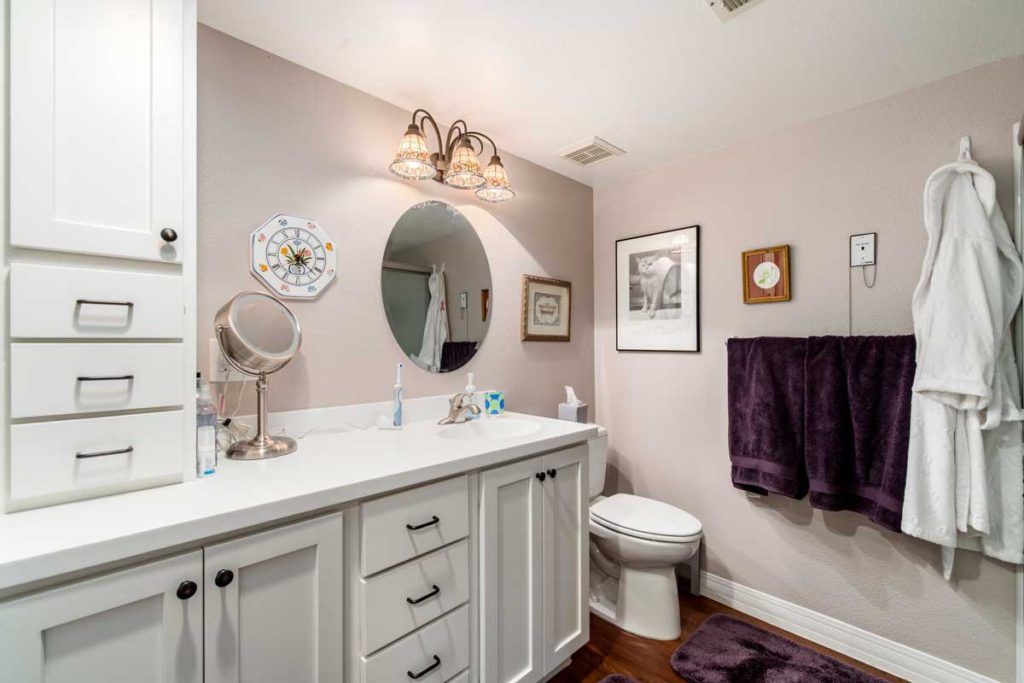 A well-lit bathroom featuring a white vanity with a large oval mirror, decorative lighting, and neatly arranged towels.