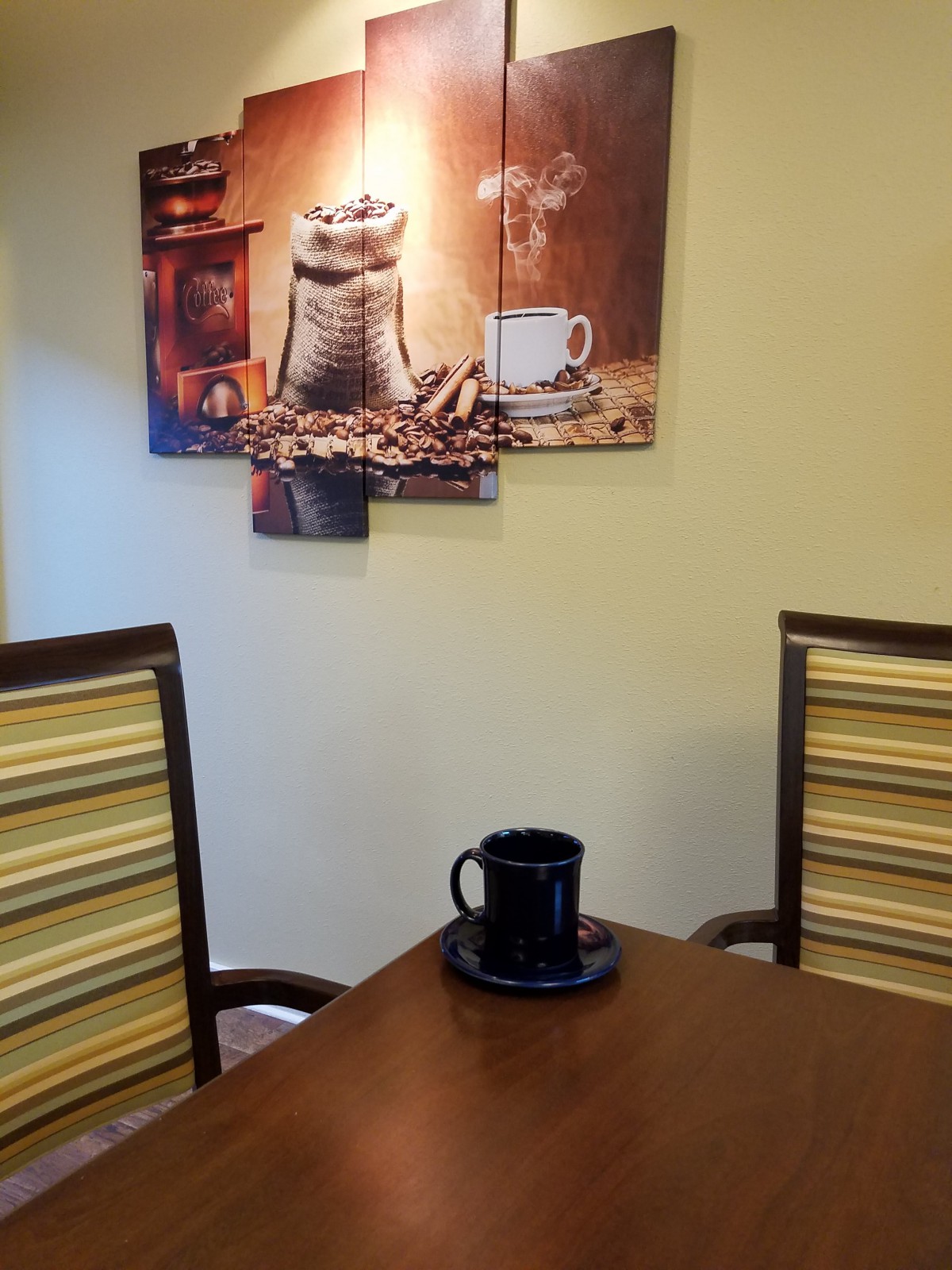 A cozy kitchen setup with a coffee-themed artwork, a table, and chairs.