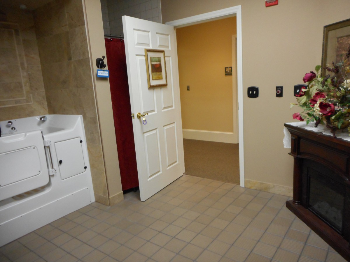 An open door leading to a warmly lit hallway from a tiled room with a sink and wall decor.