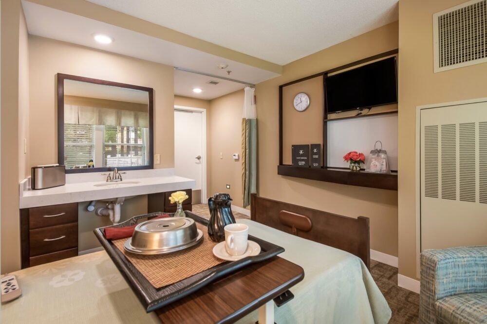 A cozy hotel room featuring a neatly arranged table with a coffee maker and tray, alongside a television mounted on the wall.