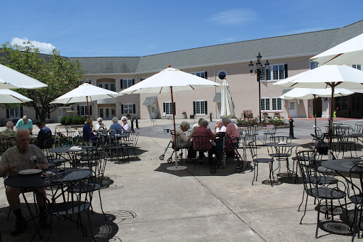A sunny outdoor patio where a group of seniors enjoys a social gathering under umbrellas.