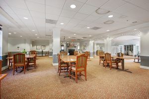 A spacious dining area with wooden tables and chairs, featuring soft lighting and carpeted flooring.