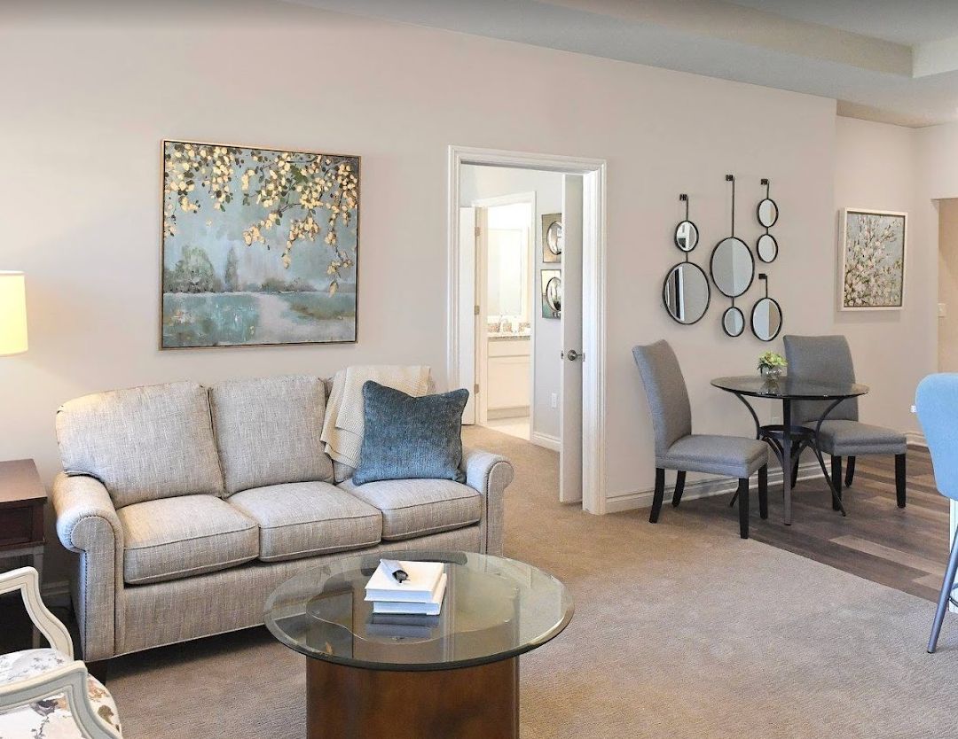 A modern living room with a cozy sofa and a glass coffee table, featuring wall art and a dining area in the background.