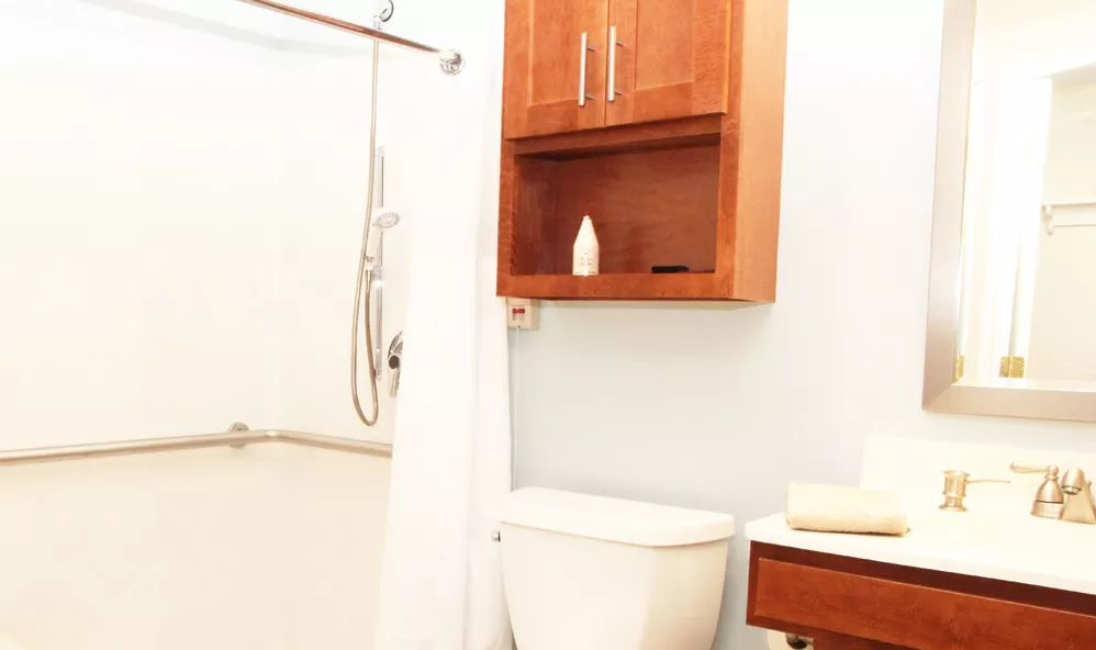 A clean and modern bathroom featuring a shower with a white curtain, a toilet, and a wooden wall cabinet.