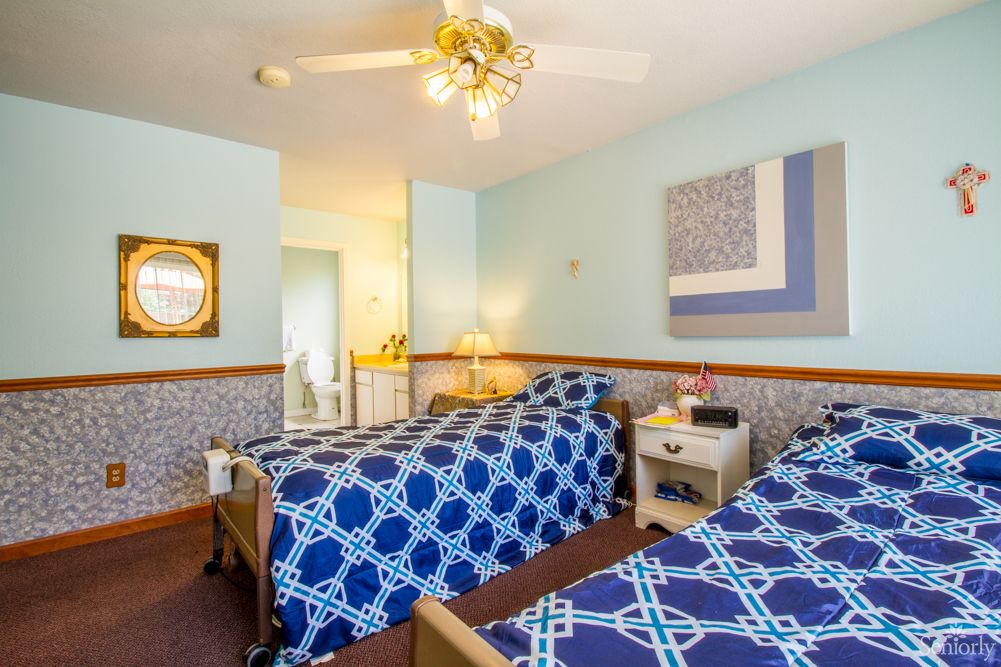 A cozy bedroom with twin beds featuring blue patterned bedding and a ceiling fan.