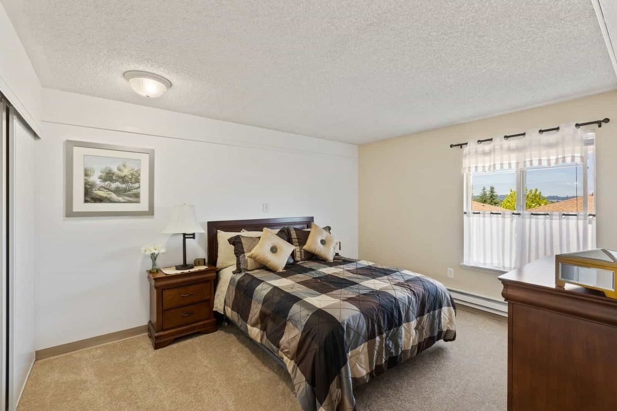A cozy bedroom featuring a neatly made bed with checkered bedding and matching nightstands, illuminated by natural light streaming through the window.