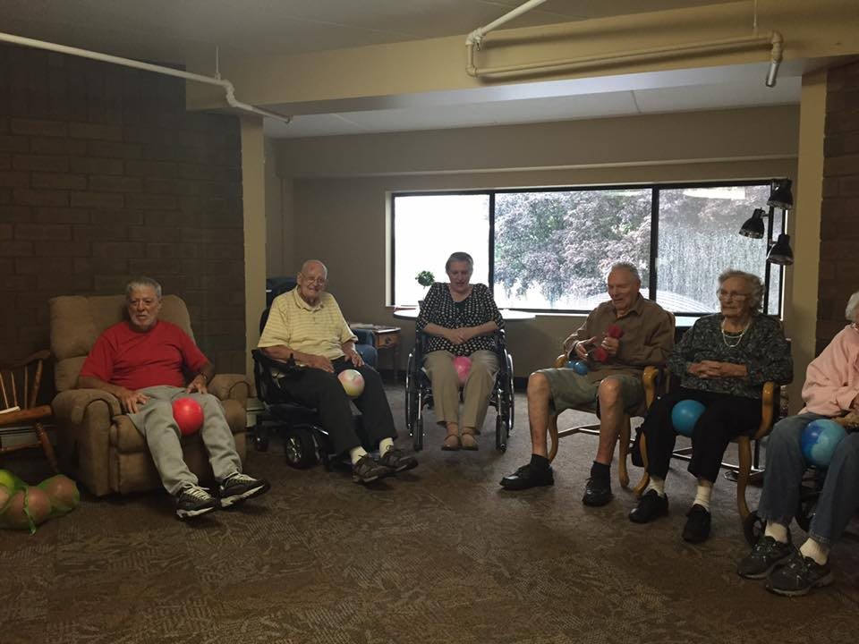 A group of elderly individuals sitting together in a room, some in wheelchairs.