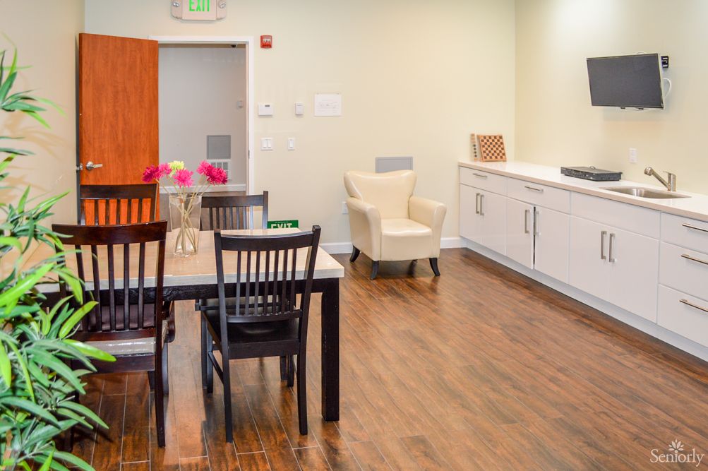 A modern dining area featuring a sleek table with black chairs, a comfortable armchair, and a compact kitchenette.