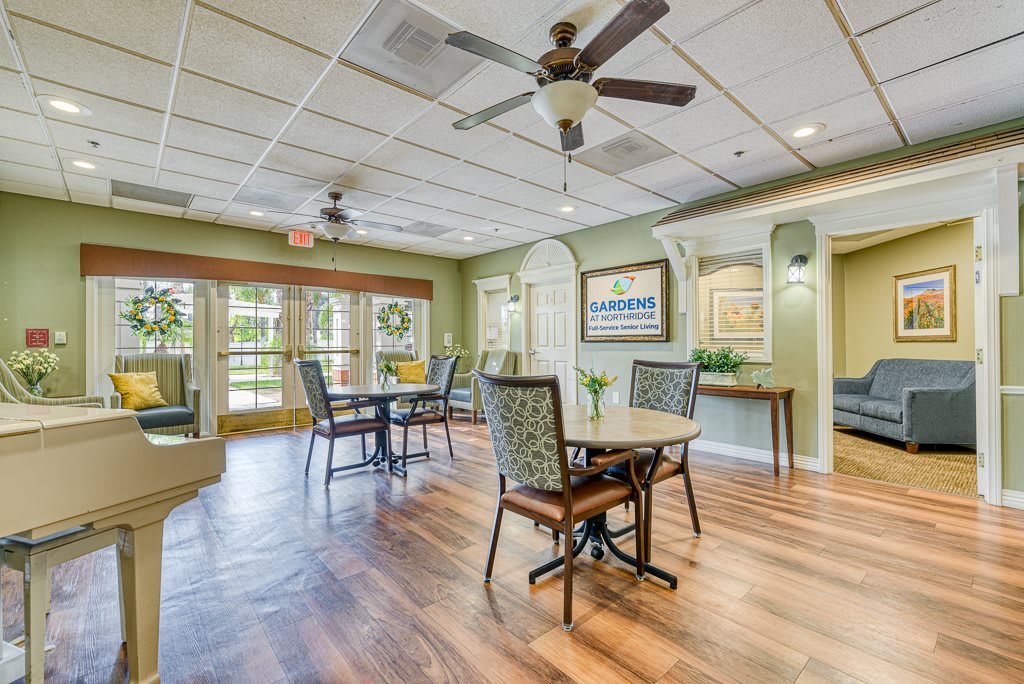 A cozy dining area with tables and chairs, featuring ceiling fans and large windows for natural light.