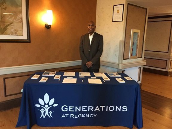 A person standing behind a table with brochures at a Generations at Regency event.