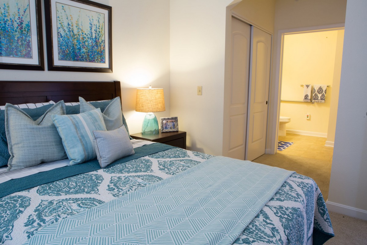 A cozy bedroom with blue and white bedding, a lamp on the nightstand, and artwork on the wall.