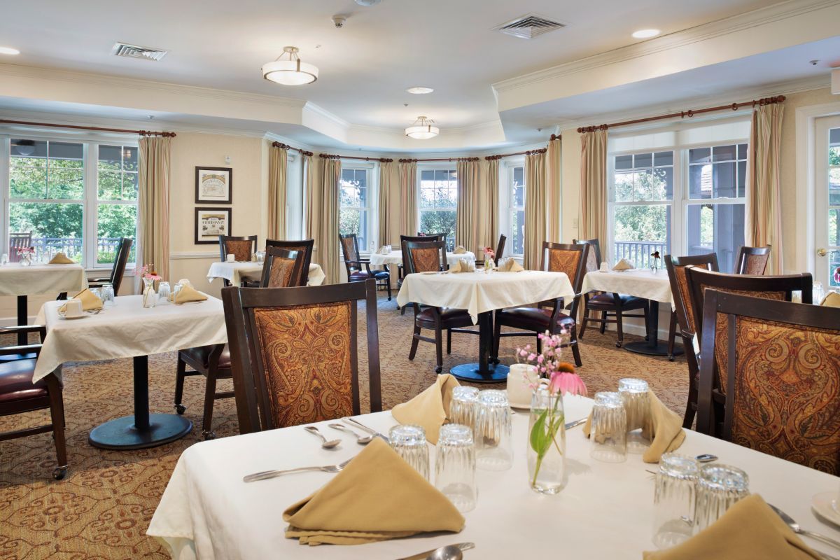 A well-decorated dining room with neatly arranged tables covered with white tablecloths and set with glasses and napkins.