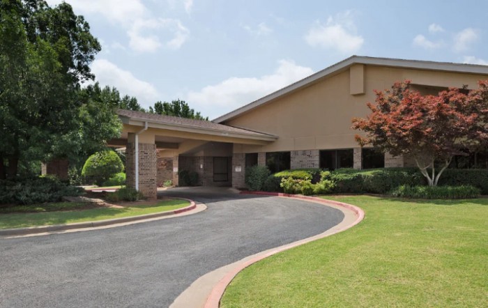 A building with a covered entrance and a curved driveway surrounded by landscaping.