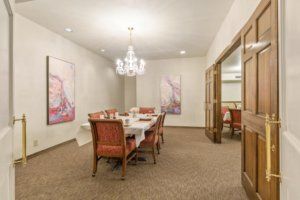 A formal dining room with elegant decor, featuring a chandelier and artwork on the walls.