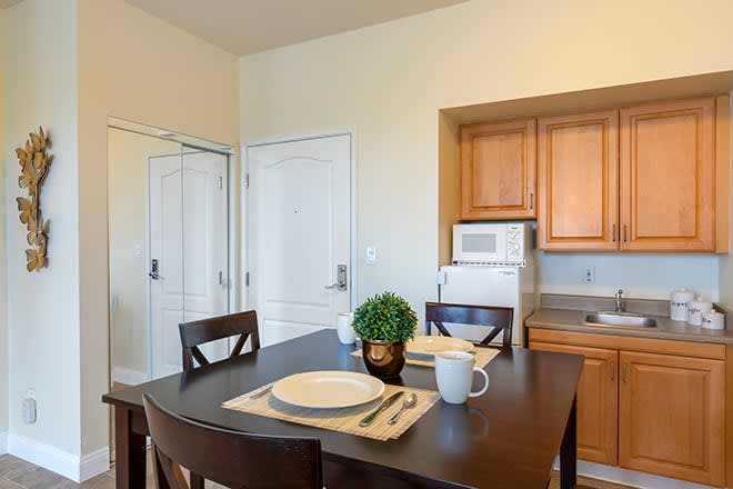 A cozy kitchen with a dining table set for two, featuring wooden cabinets and a microwave.