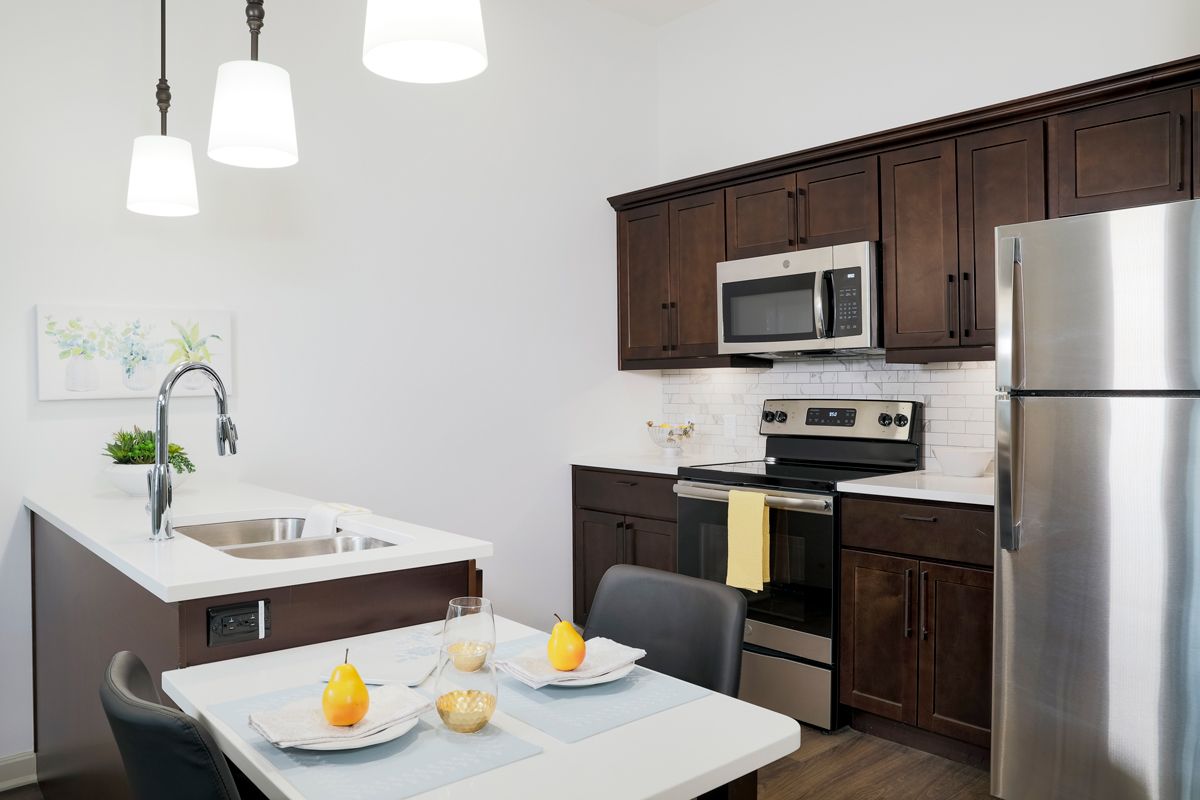 A modern kitchen with wooden cabinets, stainless steel appliances, and a small dining area.