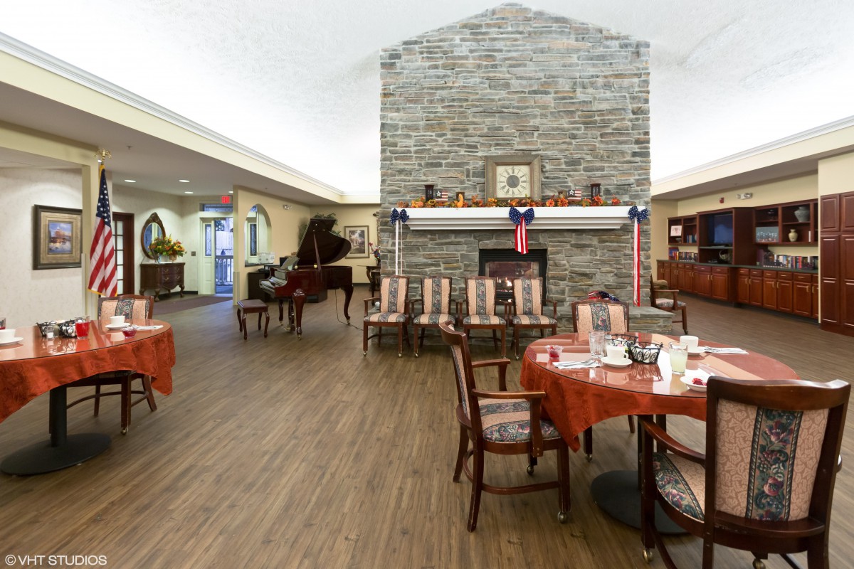 A cozy dining area with a central fireplace and red-themed decor, featuring multiple tables set for dining and a piano in the background.