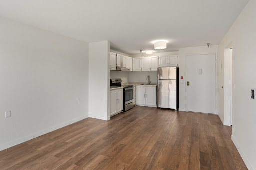 A modern kitchen area featuring white cabinetry and wood flooring, perfect for a cozy apartment.