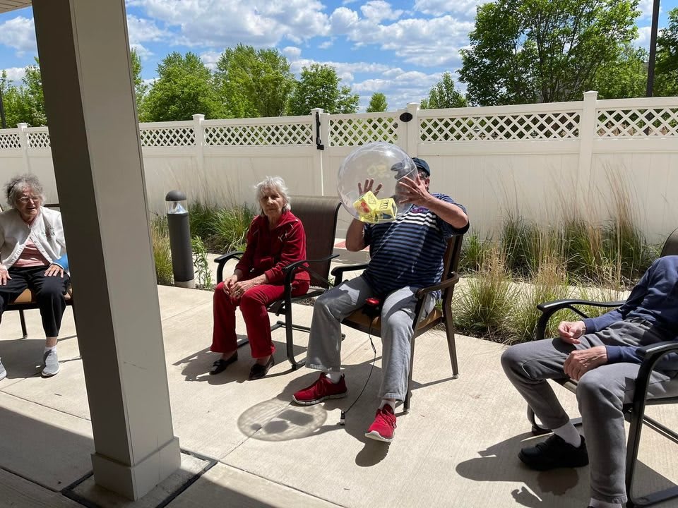 A group of people relaxing on a sunny patio, seated on chairs near a white fence.
