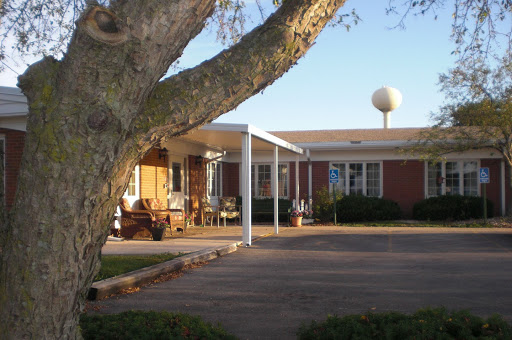 A cozy residential building surrounded by trees, featuring a well-maintained parking area under a clear blue sky.