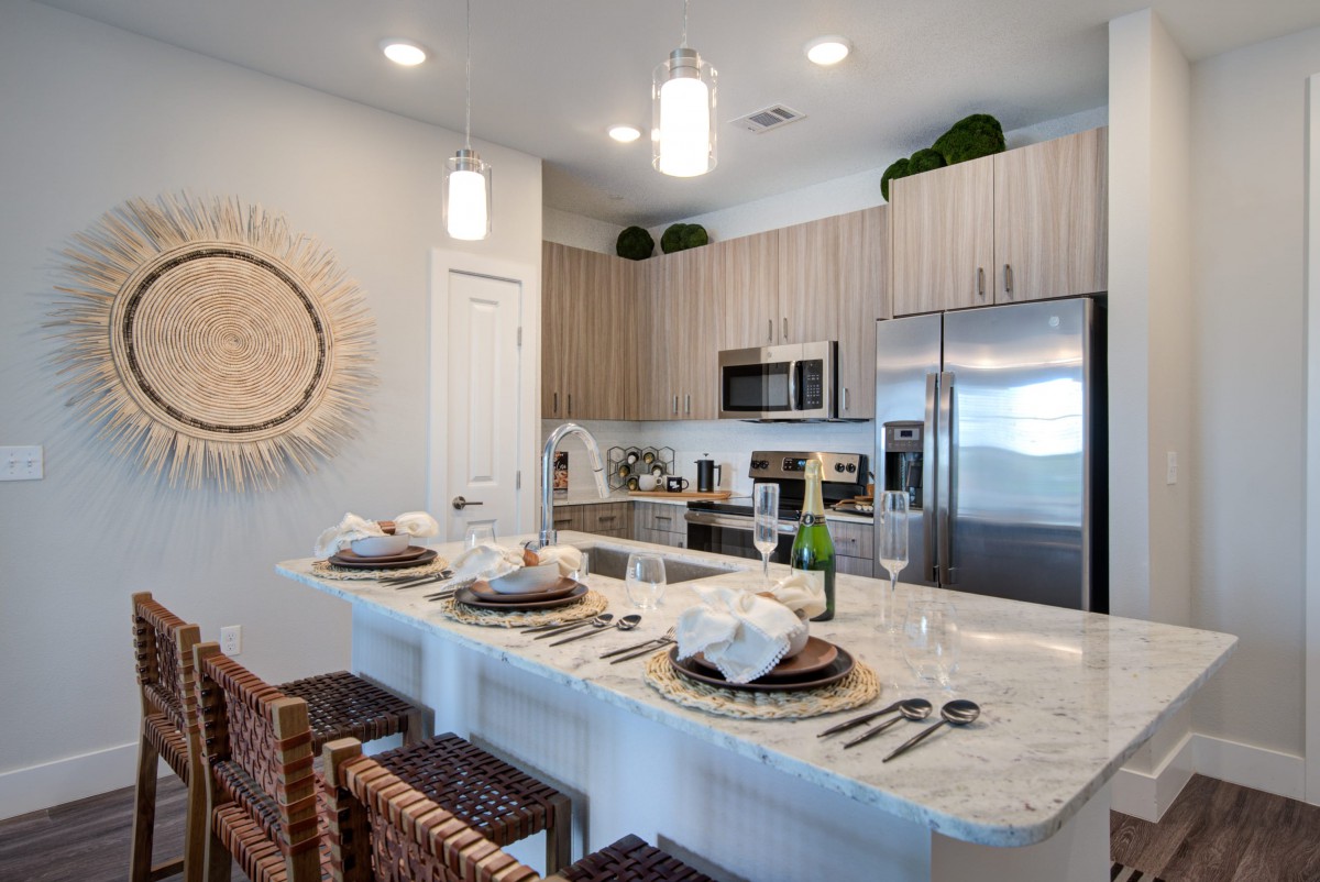 A modern kitchen with a sleek design featuring stainless steel appliances, a marble countertop with bar seating, and decorative elements.