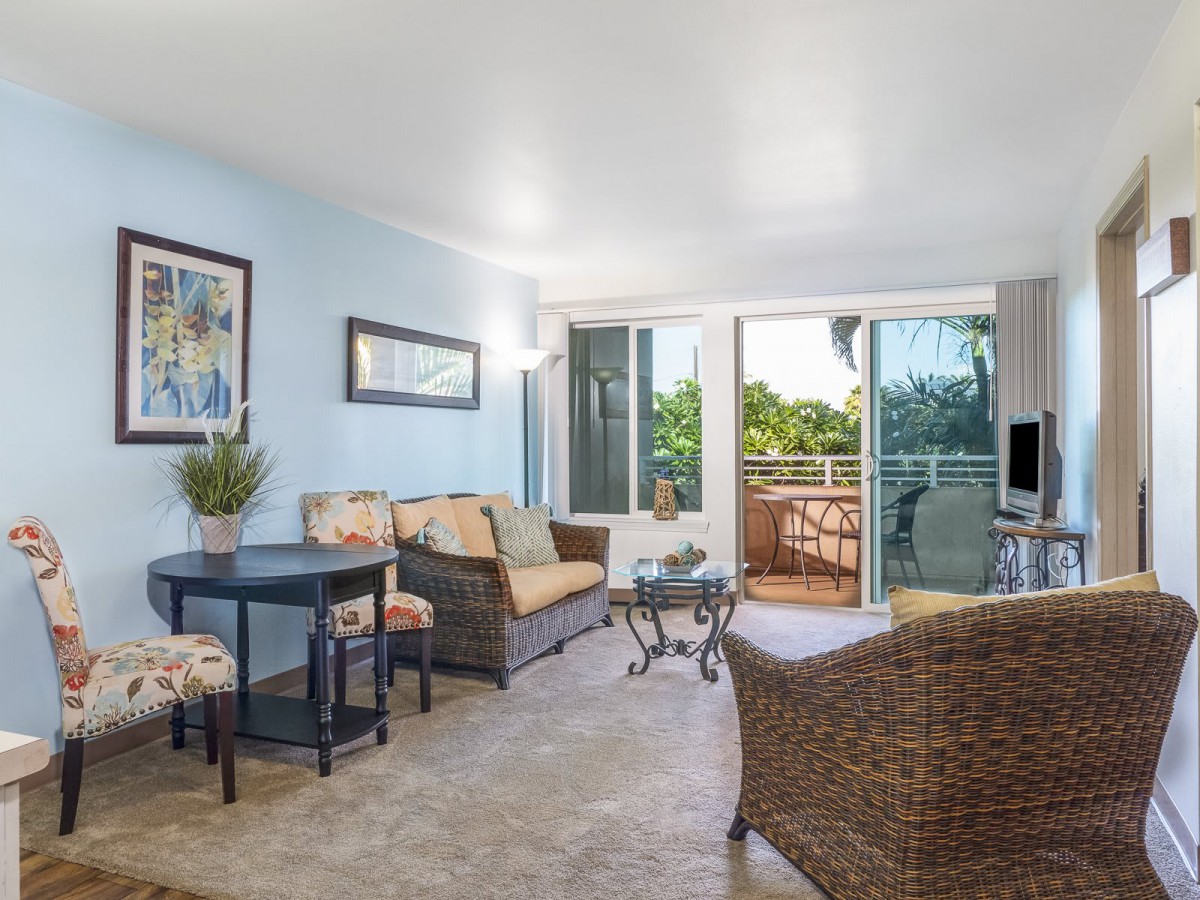 A cozy living room with wicker furniture and a balcony opening to lush greenery.