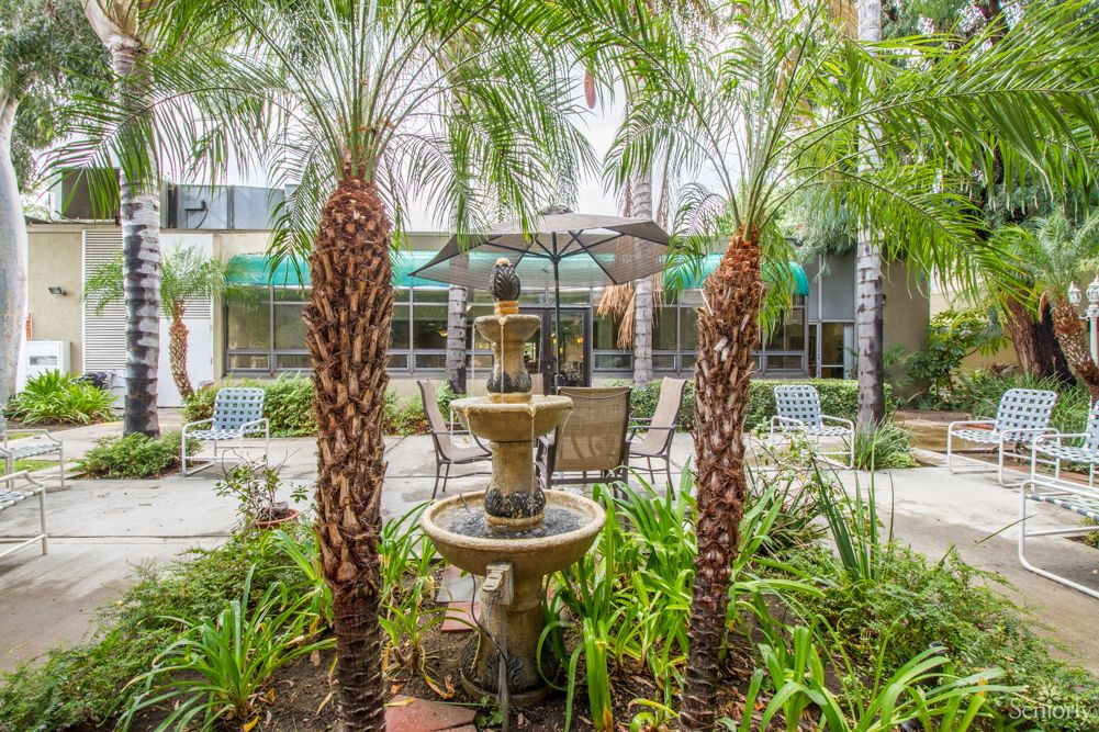 A tranquil garden setting featuring a multi-tiered fountain surrounded by lush palm trees and outdoor seating.