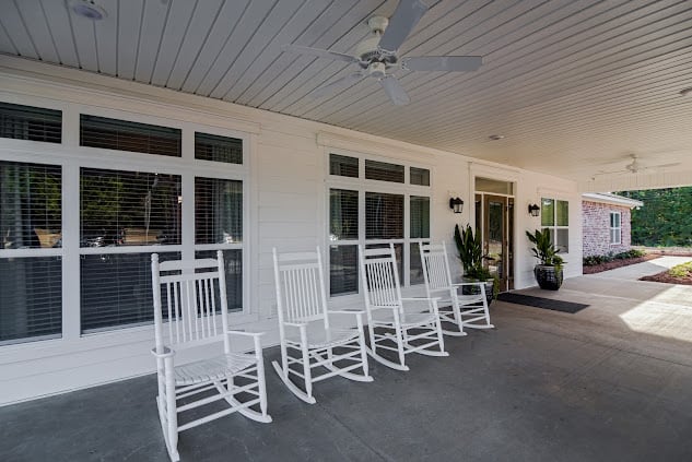 A cozy porch with white rocking chairs and potted plants.