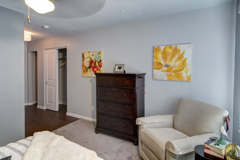 A cozy bedroom corner with a dark wooden chest of drawers, a comfortable chair, and colorful artwork on the walls.
