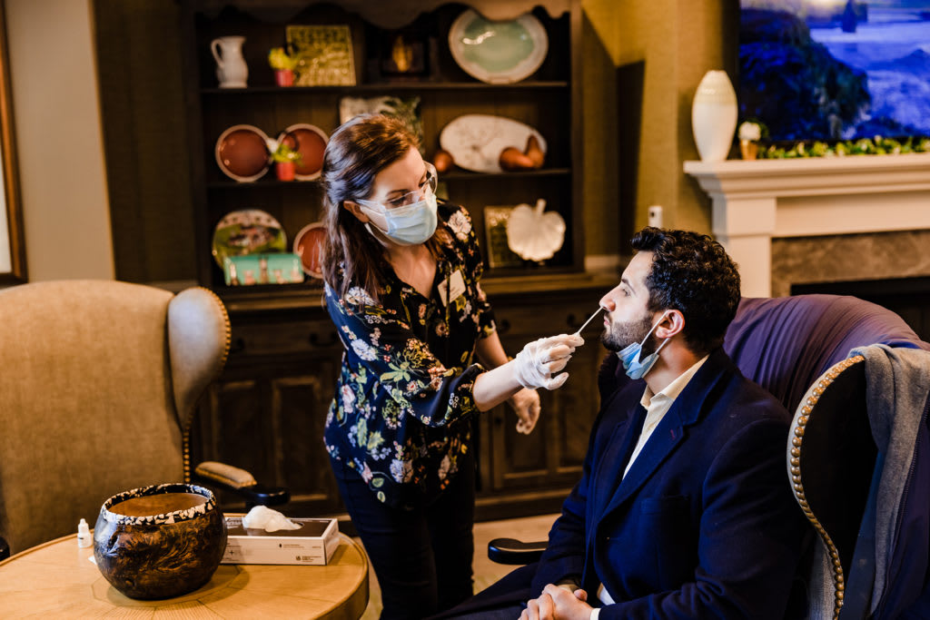 A healthcare worker administers a COVID-19 test indoors, both wearing masks for safety.