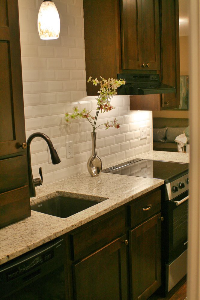 A modern kitchen with a sleek countertop, featuring a sink, stove, and elegant backsplash.