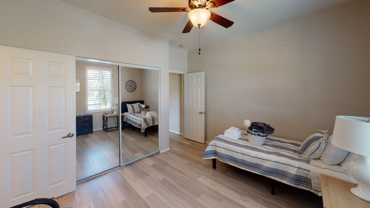A modern, minimalist bedroom with a single bed, mirrored closet doors, and wood flooring illuminated by natural daylight.