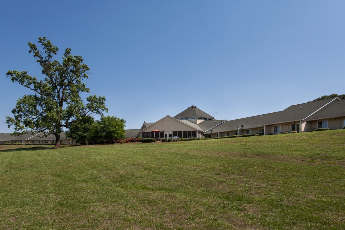 A large building with a sloping roof surrounded by an expansive lawn and trees under a clear blue sky.