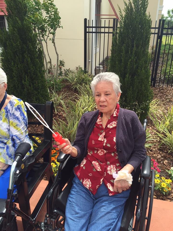 Two elderly women sitting in wheelchairs outdoors, enjoying a day in the garden while blowing bubbles.