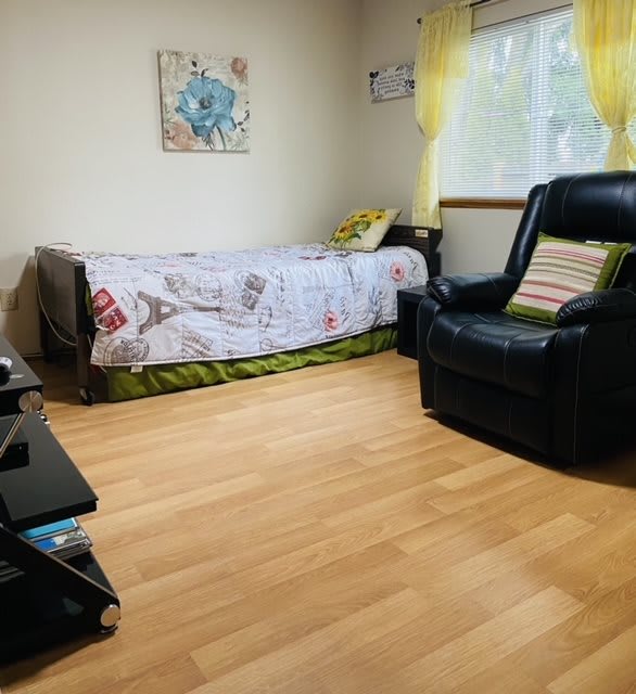A cozy bedroom with a single bed and armchair beside a sunlit window.