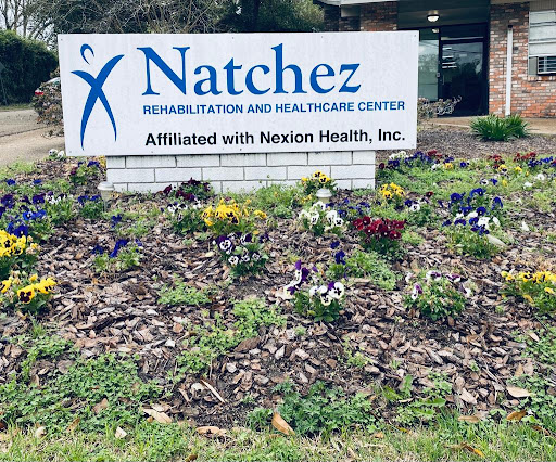 Sign for Natchez Rehabilitation and Health Care Center, surrounded by colorful flowers.