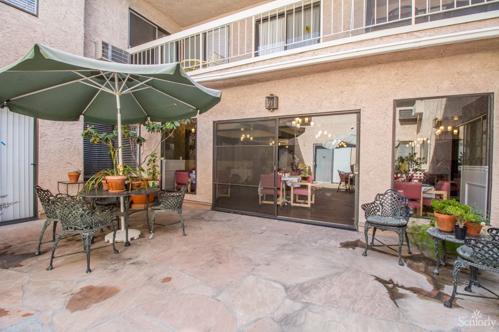 A cozy patio with outdoor furniture and potted plants, featuring a table with an umbrella and seating.