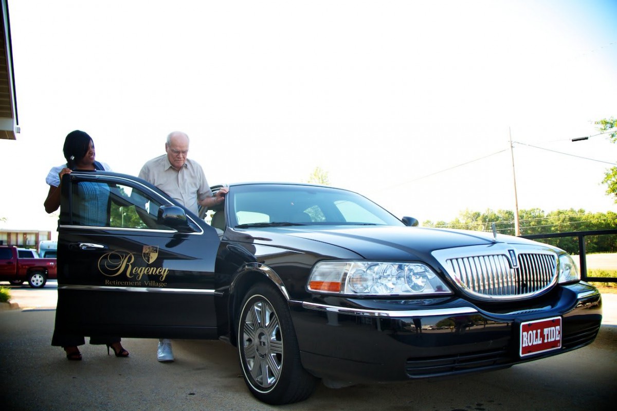 A man standing beside a luxury black limousine outdoors.