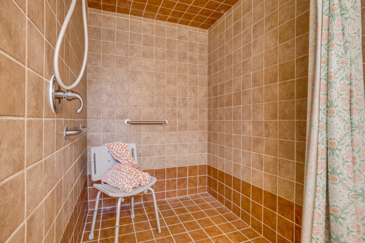 An accessible walk-in shower with tiled walls and a shower chair.
