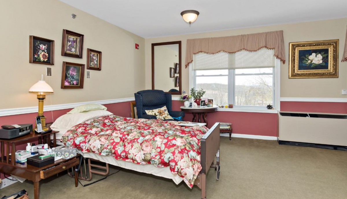 A cozy bedroom with a floral bedspread, armchair, and large window.