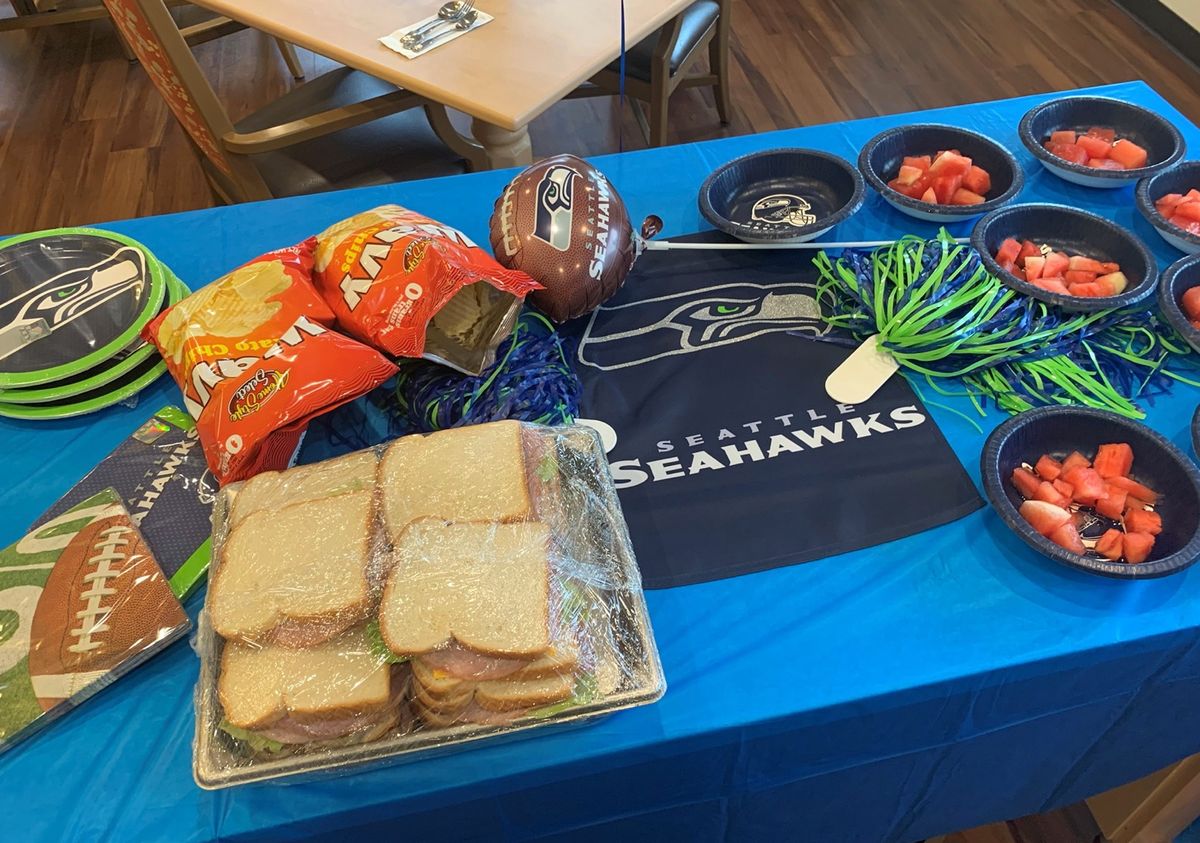 A Seattle Seahawks-themed table setup with sandwiches, chips, and snacks.