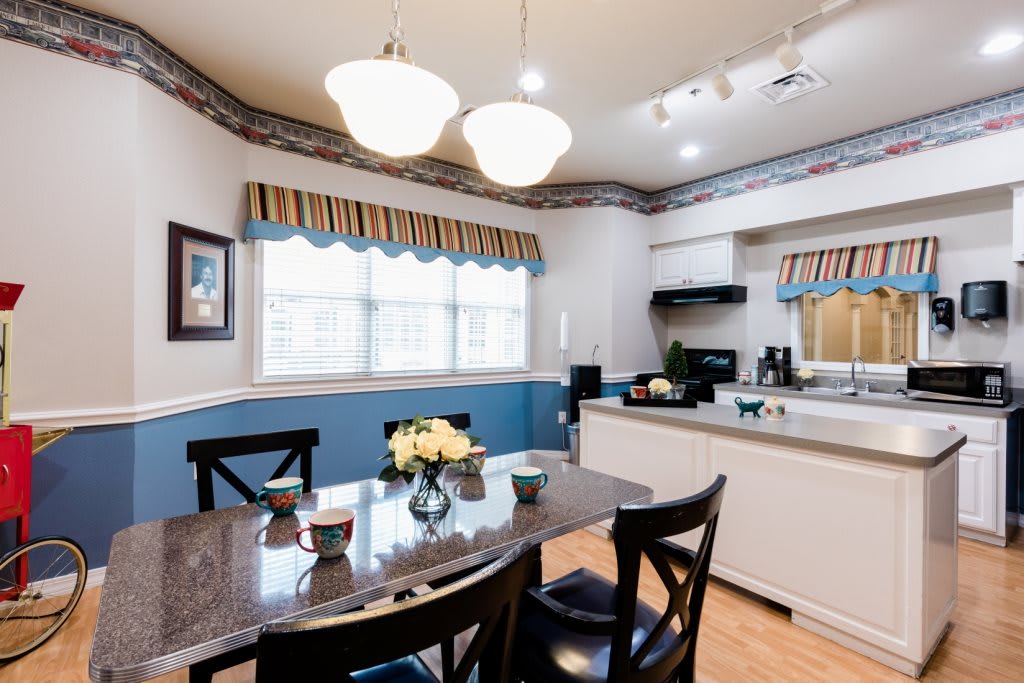 A cozy kitchen and dining area with a table set for four, bright lighting, and large windows with curtains.