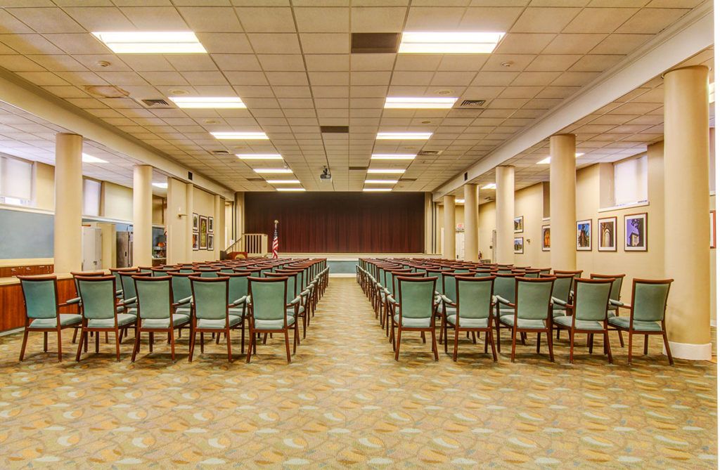 An empty auditorium with rows of chairs facing a stage.