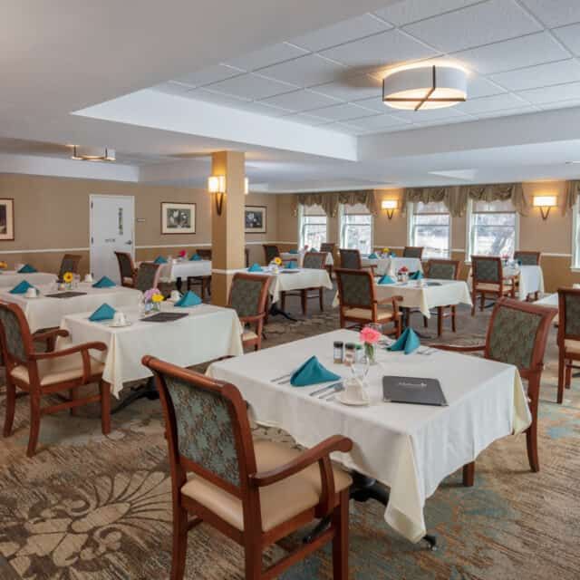 An elegant dining room with neatly arranged tables and chairs, adorned with blue napkins and tasteful decor.