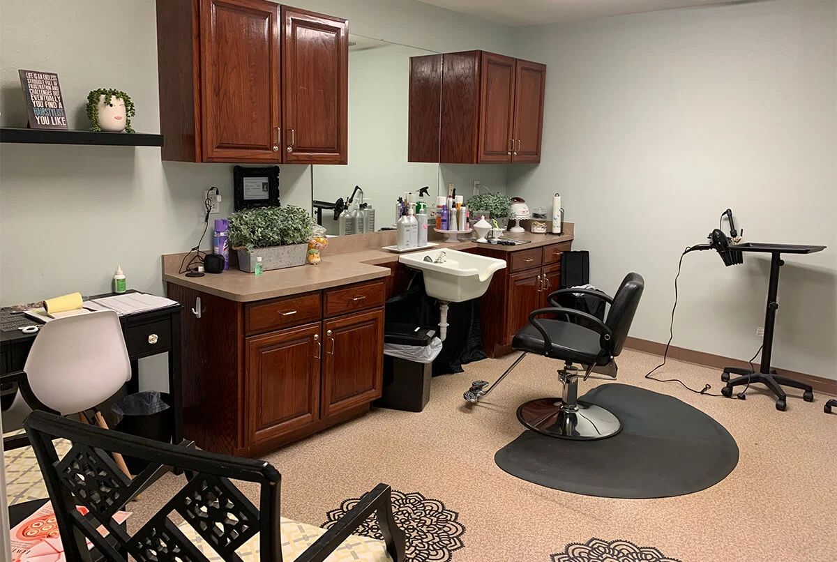 A cozy hair salon setup with a barber chair, mirror, and cabinets filled with beauty products.