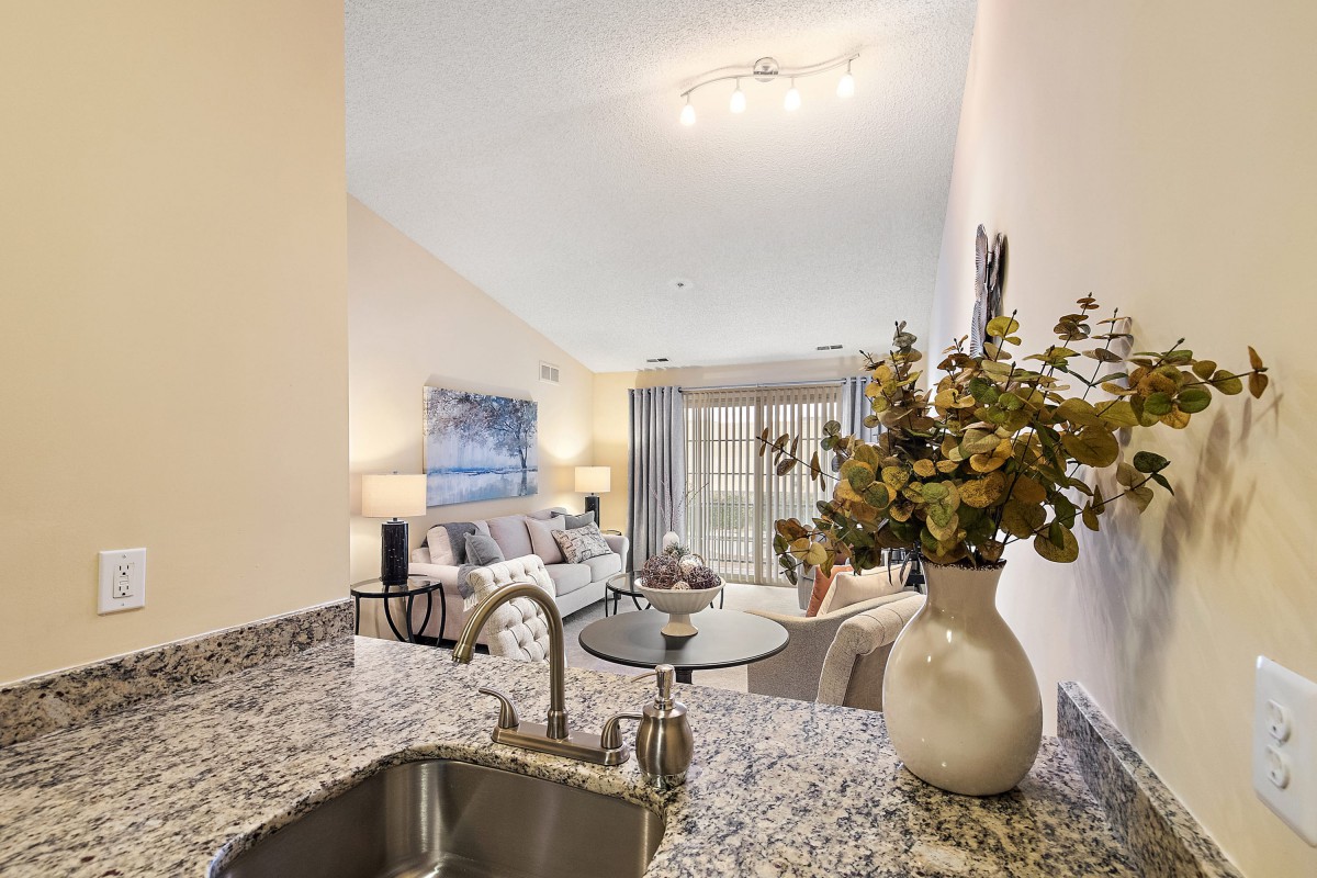 A modern open-plan living area featuring a stylish kitchen with granite countertops and a cozy living room adorned with neutral tones and decorative flowers.